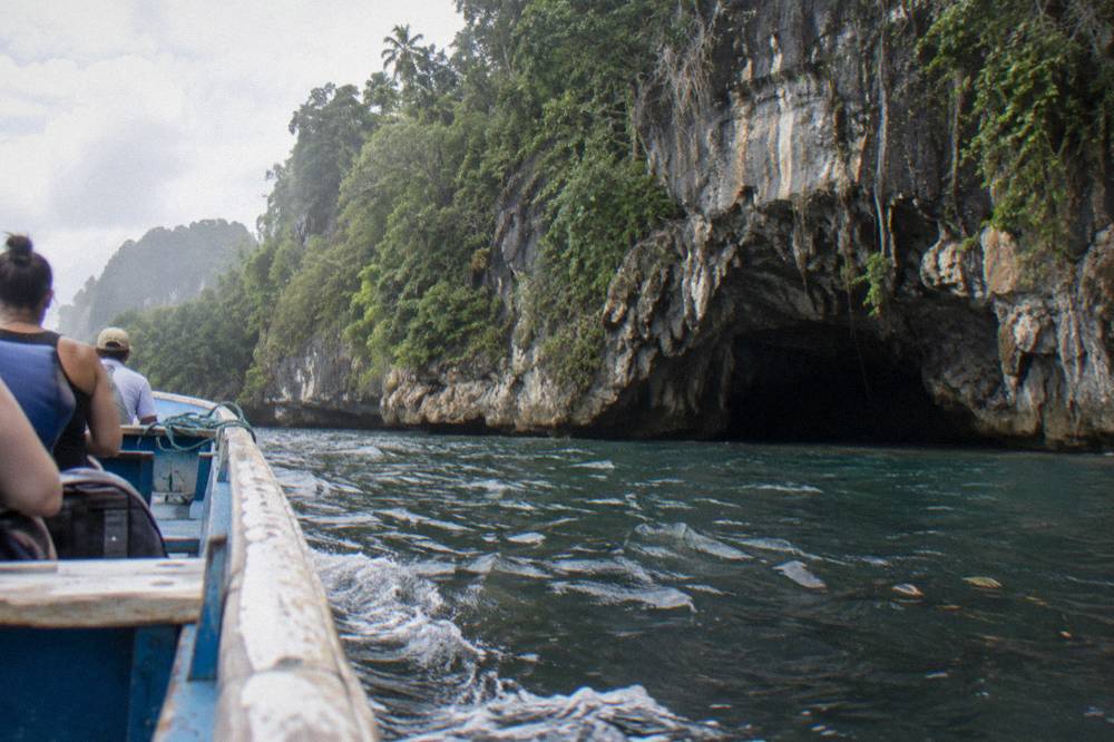 Wooden boat approaching a cave entrance in the limestone cliffs of Los Haitises