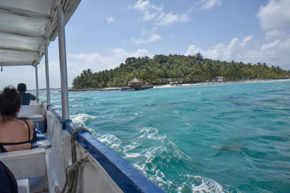 A tour boat crossing calm turquoise water toward a palm-covered island