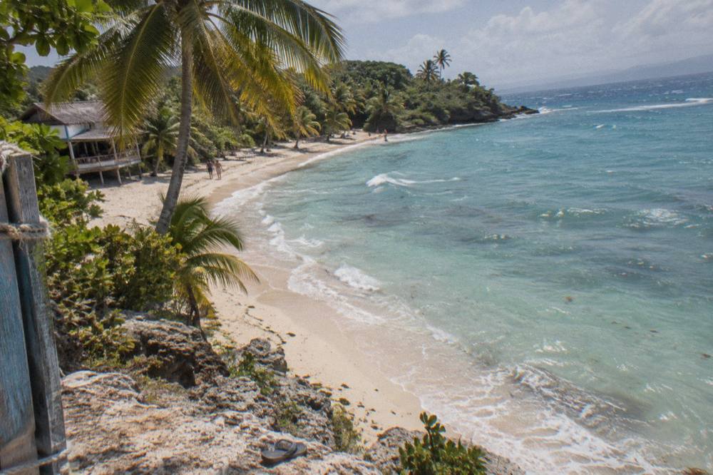 A small palm covered island with white sand beach seen across calm turquoise bay water