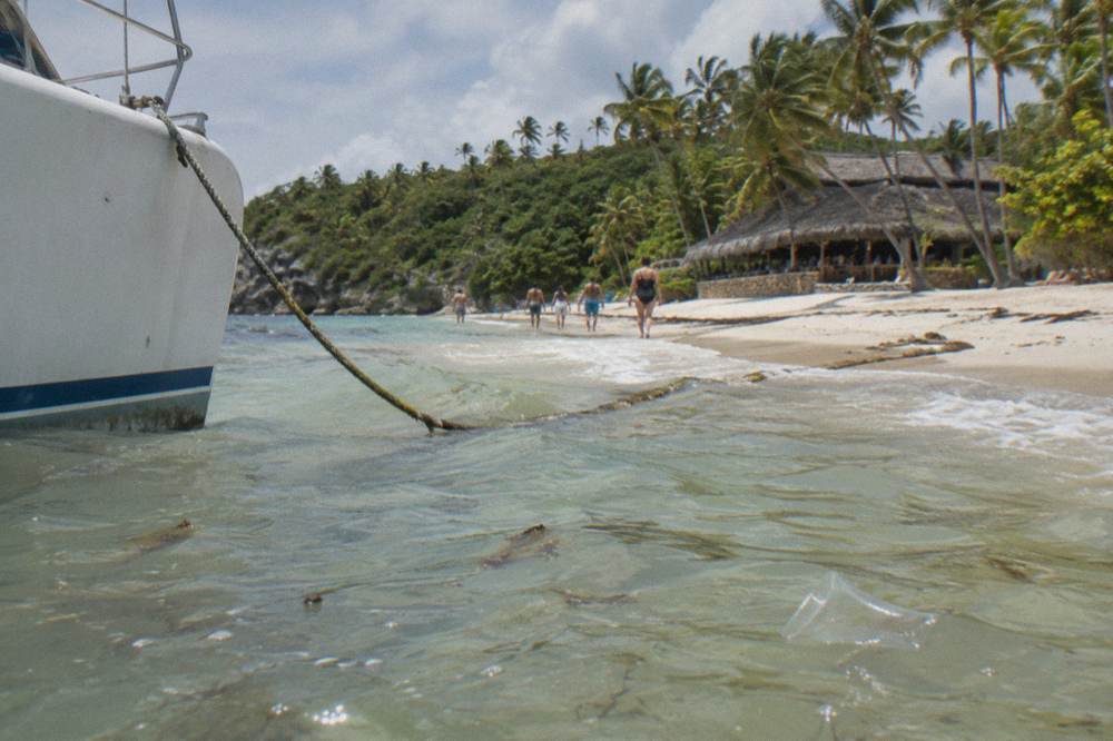 A catamaran anchored near a white sand island beach with passengers wading ashore