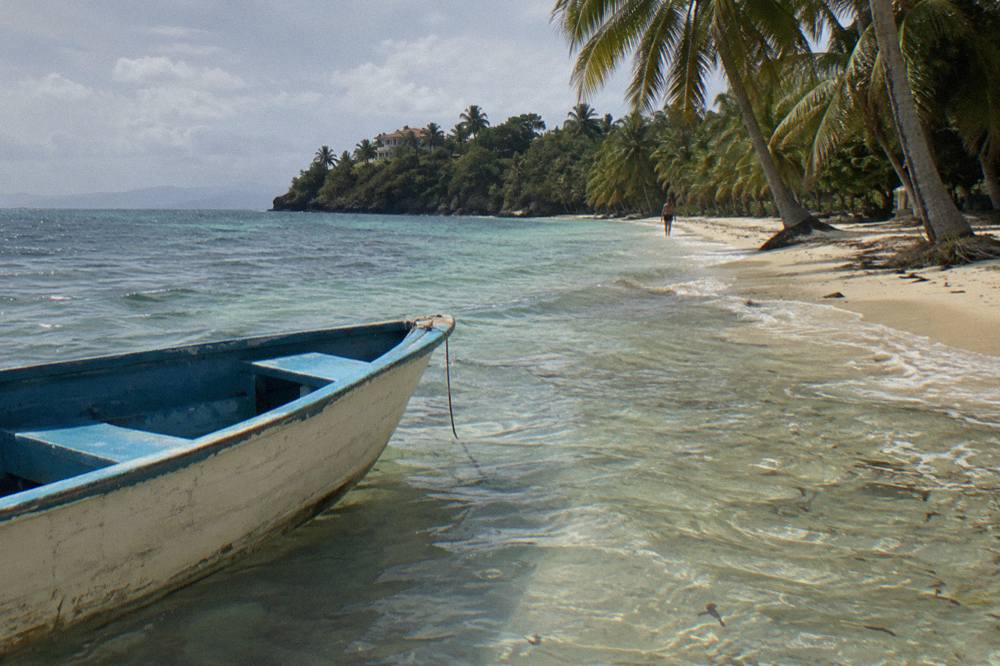 Wooden boat moored in clear shallow water beside a palm fringed white sand beach