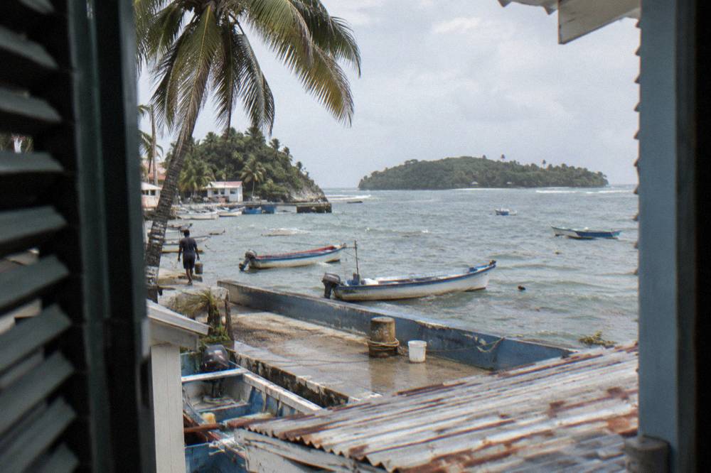 Waterfront guesthouses along a bay promenade with fishing boats at anchor