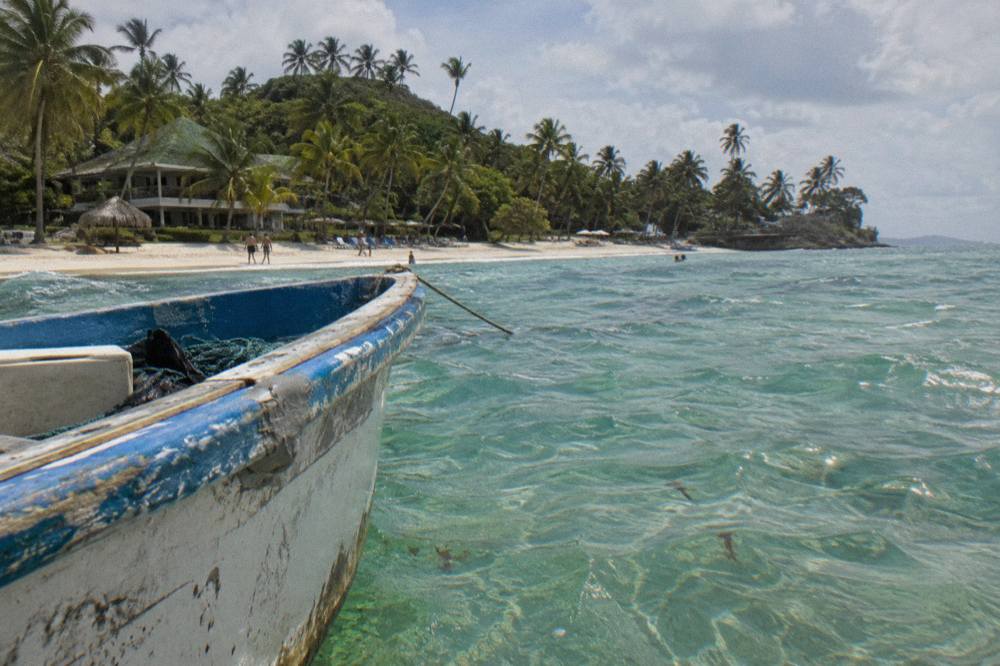 Wooden boat anchored near a palm-fringed island beach in Samana Bay