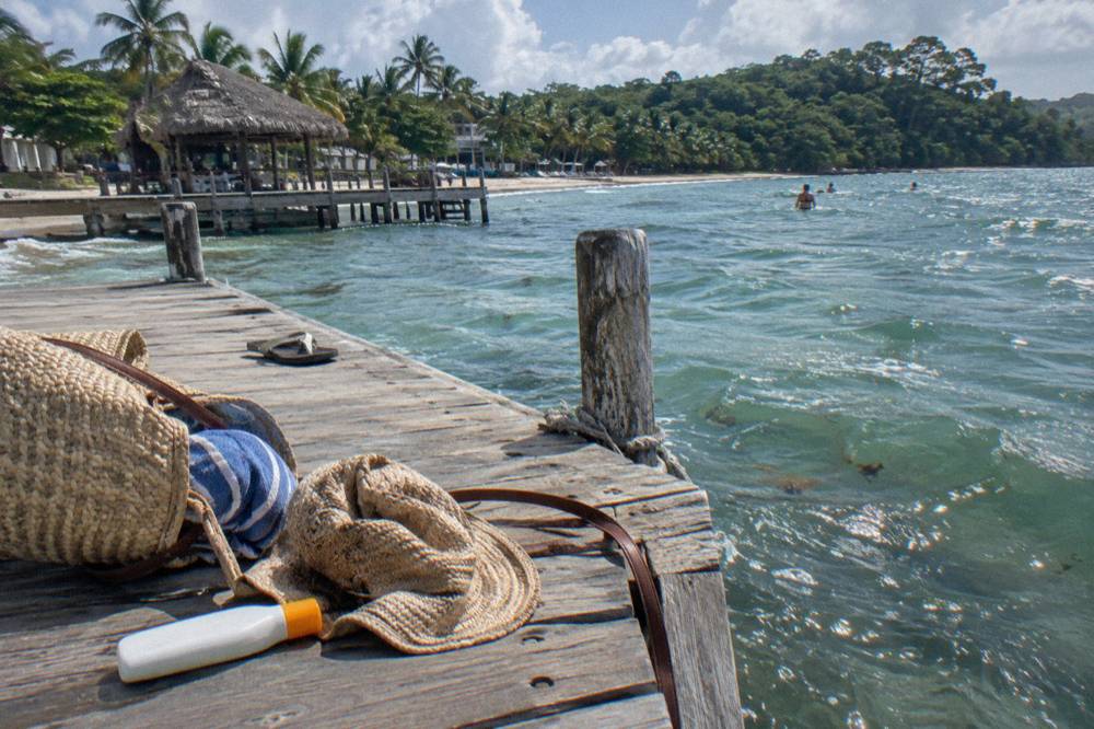 A tote bag with a sun hat, towel and sunscreen on the slats of a pier