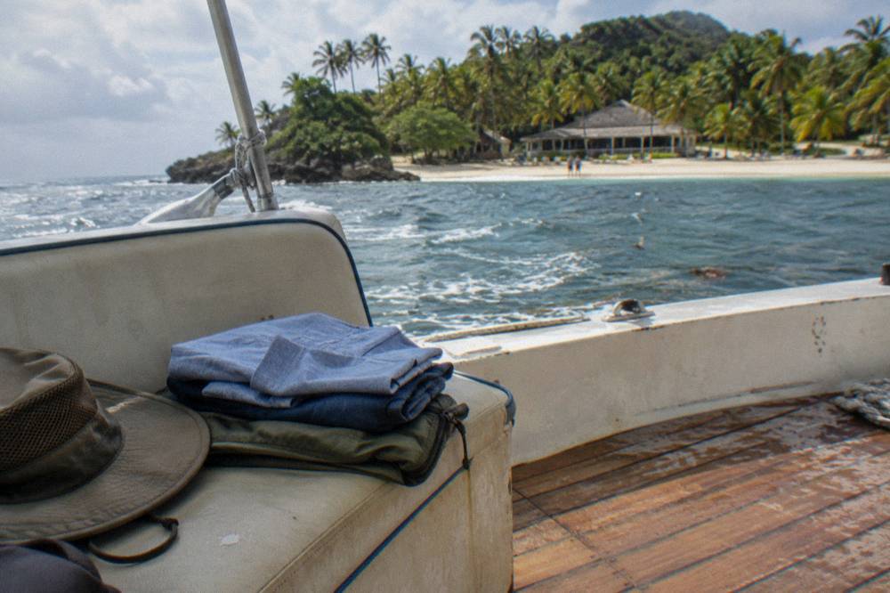 Folded quick dry shirts and a windbreaker stacked on a boat seat with a sun hat