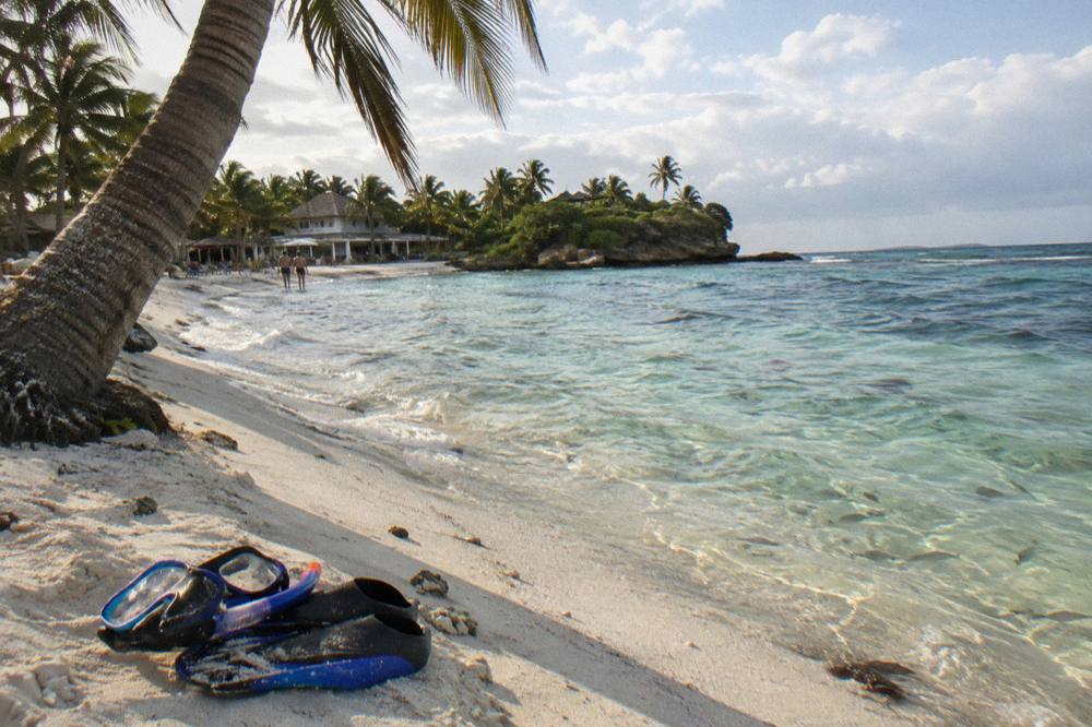 A snorkel mask and fins resting on white sand beside calm clear water