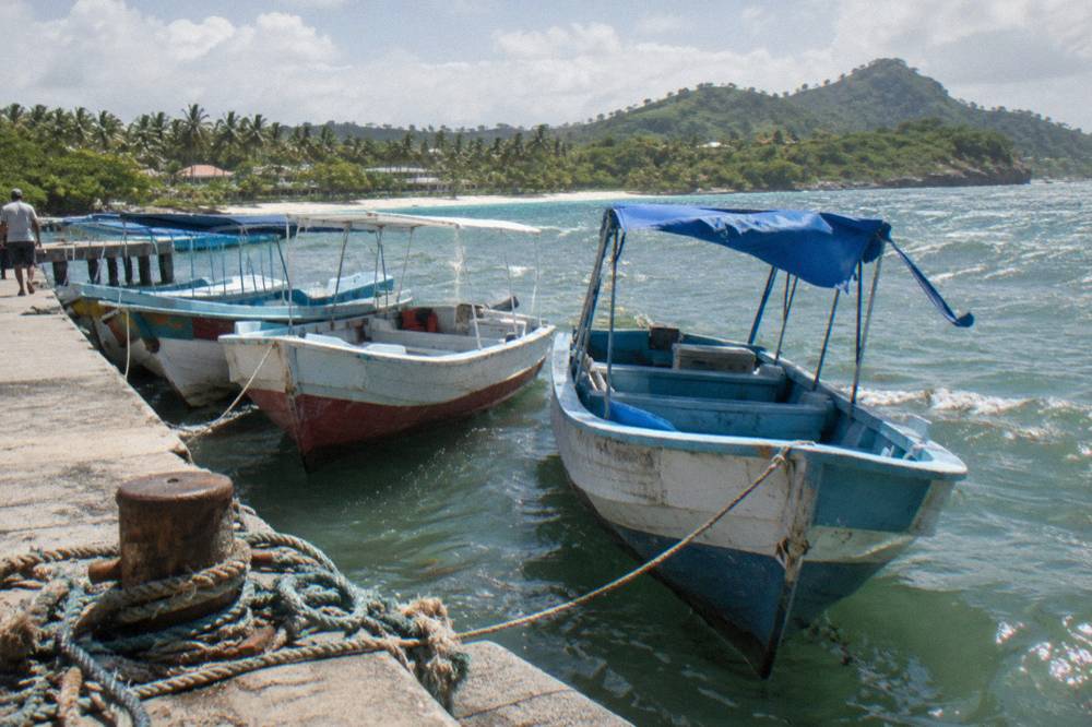 Wooden tour boats tied at a dock with calm green water and hills behind